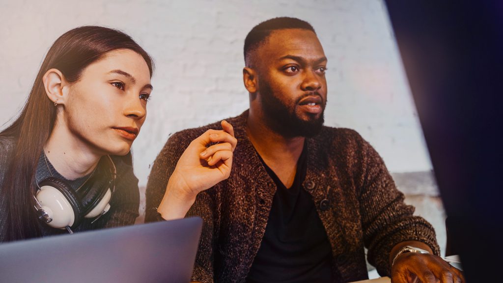 En kvinna med långt hår och hörlurar runt halsen sitter tillsammans med en korthårig man och tittar mot någonting som vi inte ser.