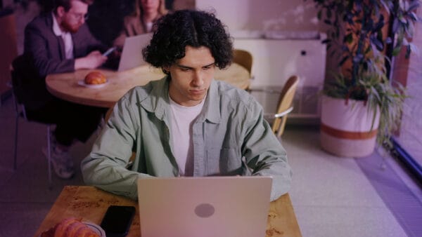 Brunhårig ung man sitter och skriver på laptop på ett café