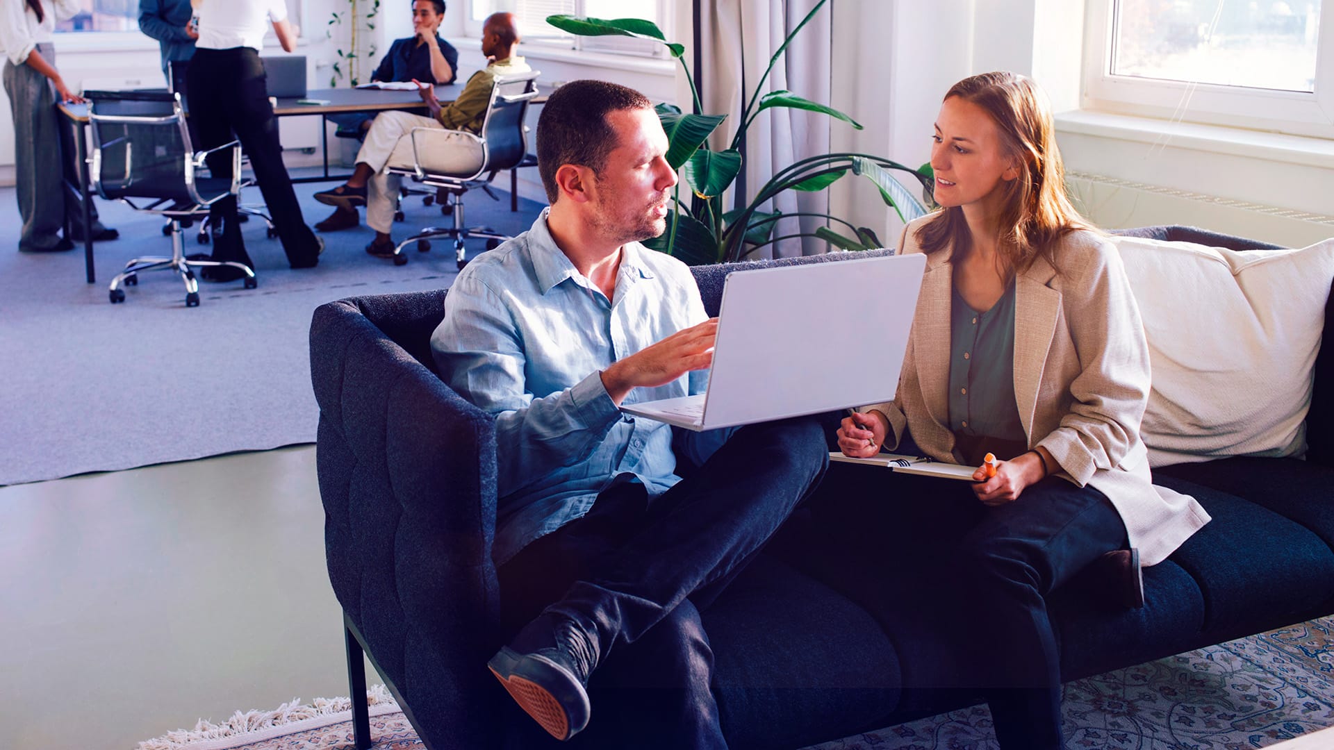 En man och en kvinna sitter i ett öppet kontorslandskap. Båda har en laptop i sina knän.