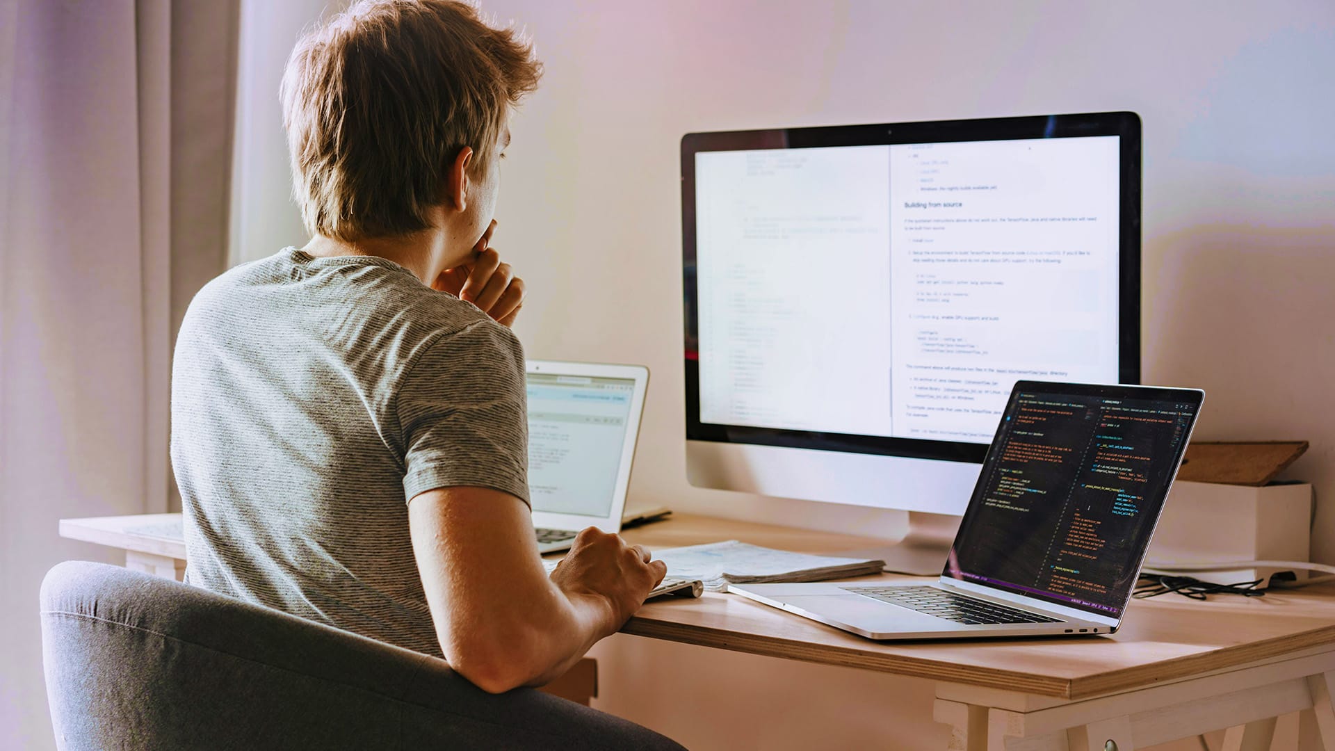 En kille sitter vid ett skrivbord med ryggen mot kameran. Han tittar på en datorskärm